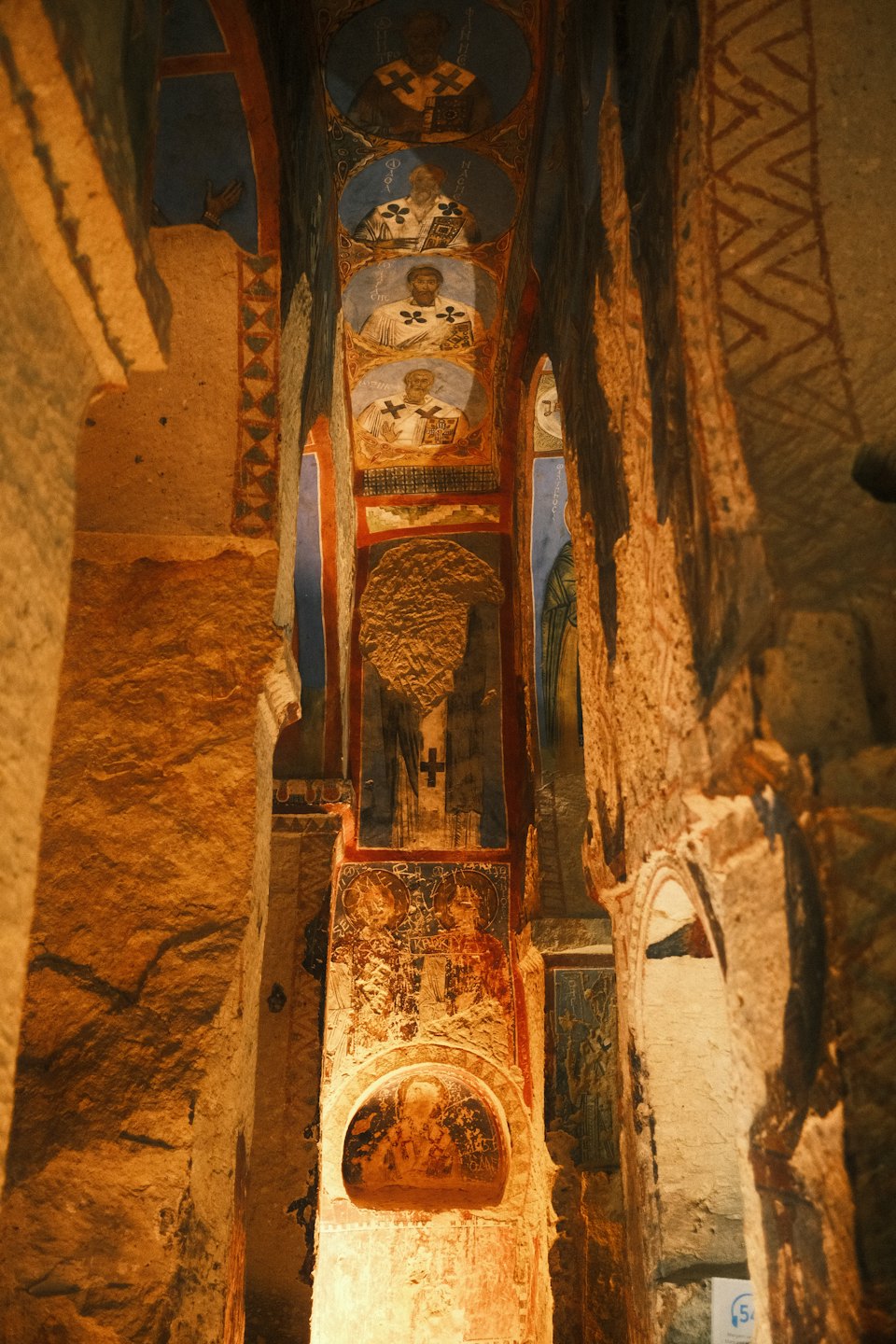 Antichi affreschi religiosi sbiaditi ricoprono le pareti di un passaggio scavato nella roccia.